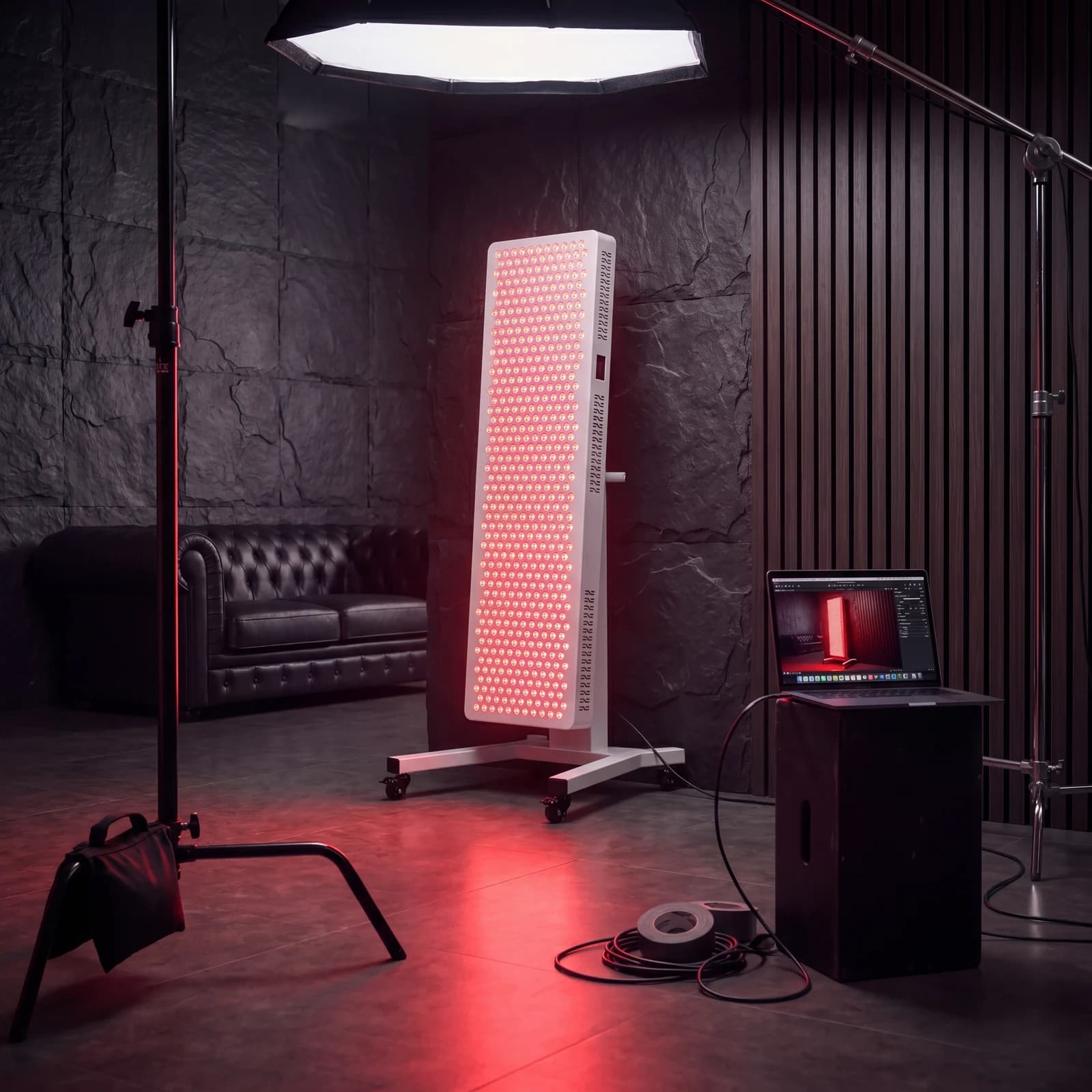 Behind-the-scenes studio shot of the RLPRO 2000 being photographed — panel powered on with LED grid glowing red, softbox + c-stand + tethered laptop in frame, dark slate stone studio